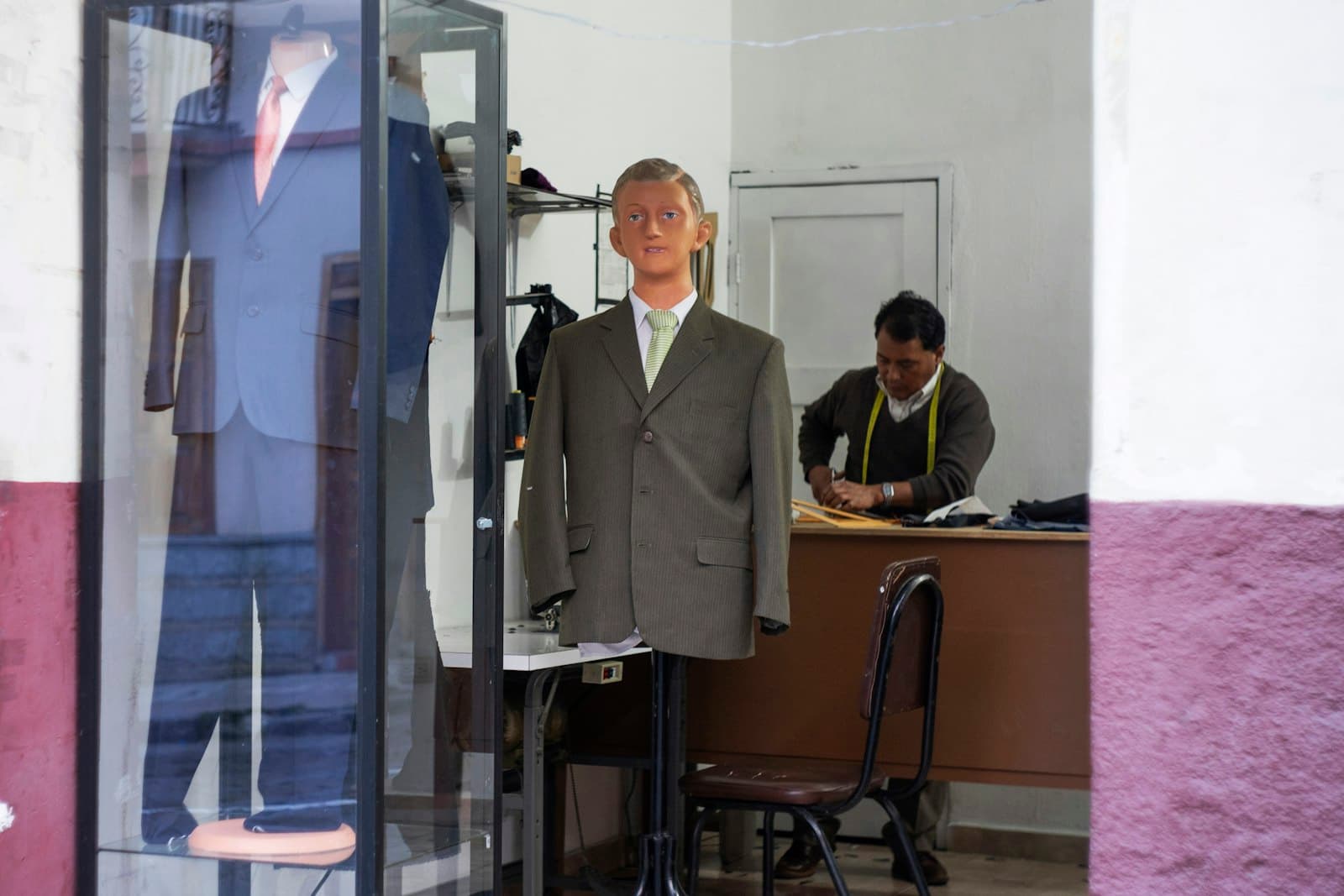 Alfaiate trabalhando atrás de um manequim na vitrine da loja